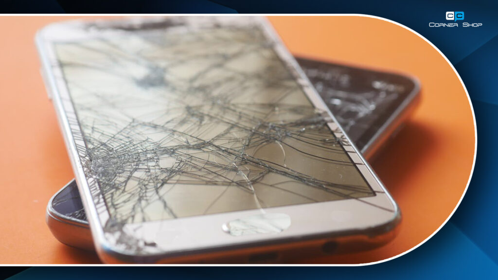 Two smartphones with severely cracked screens stacked on an orange surface